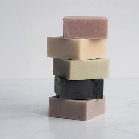 Makana Botanical Bar Soaps in various scents stacked on white marble background